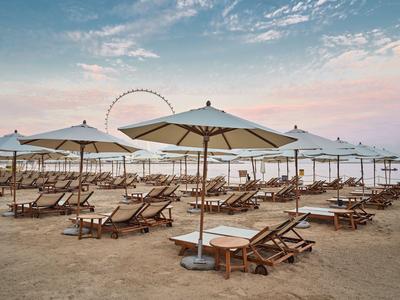 Leere Strandliegen und Sonnenschirme am Sandstrand bei Dämmerung mit Riesenrad im Hintergrund.