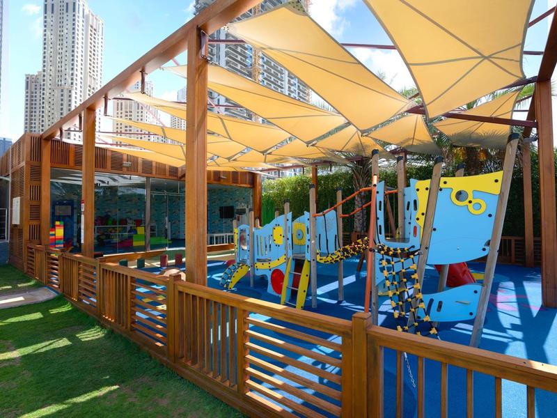 Parque infantil moderno cubierto con equipos coloridos y barandilla de madera en un parque urbano.