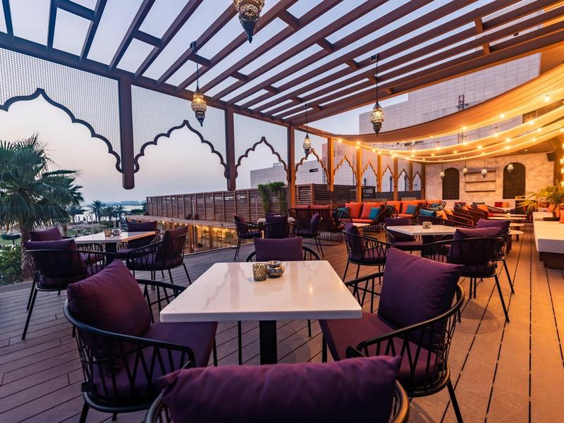 Cómodo lounge en una terraza cubierta del hotel con áreas para sentarse y iluminación ambiental.