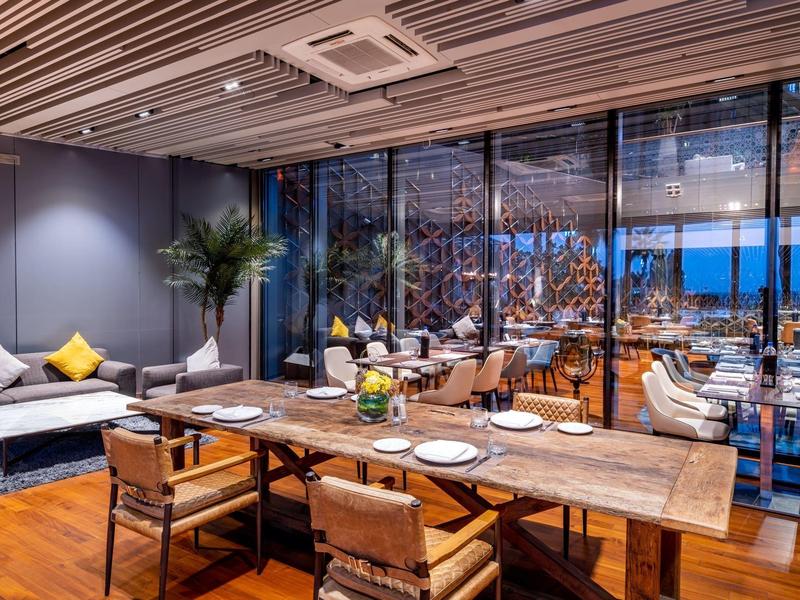 Mesa de comedor moderna de hotel con muebles de madera y área lounge de noche con vista al mar.