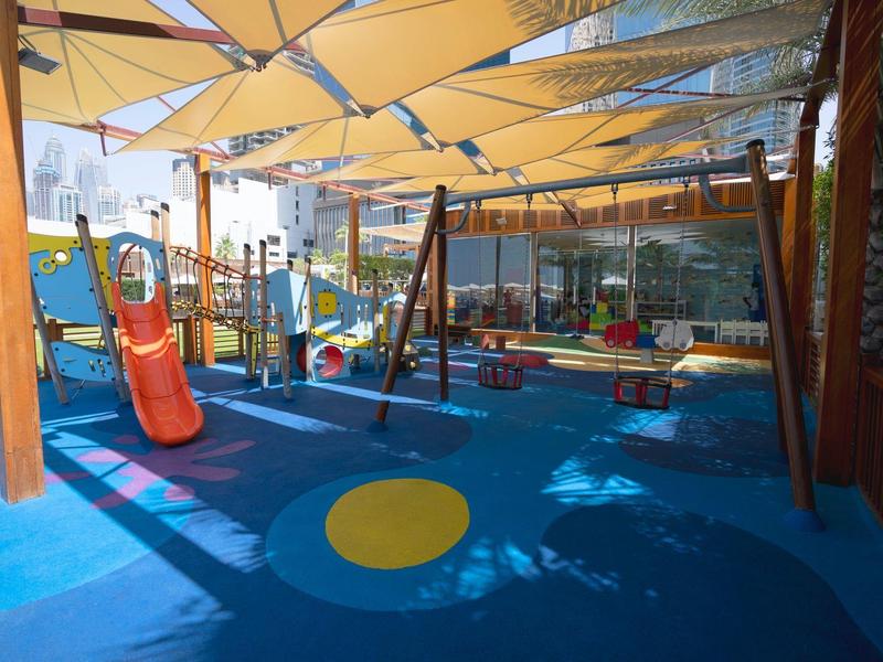 Área de juegos colorida para niños con tobogán y columpio, cubierta por toldos amarillos.