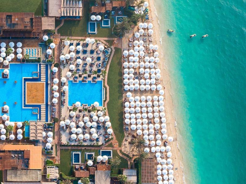 Vista aérea de un resort con piscinas y sombrillas en la playa junto al mar turquesa.