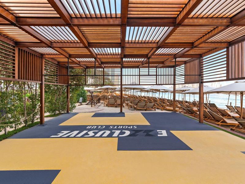 Área exterior cubierta de un hotel con tumbonas y paredes laterales verdes.