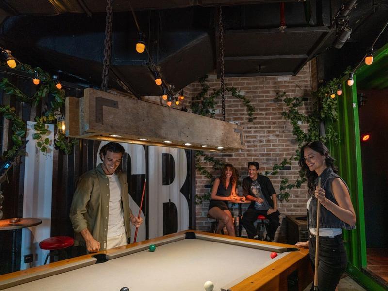 Personas jugando en una sala acogedora con mesa de billar y luces cálidas.