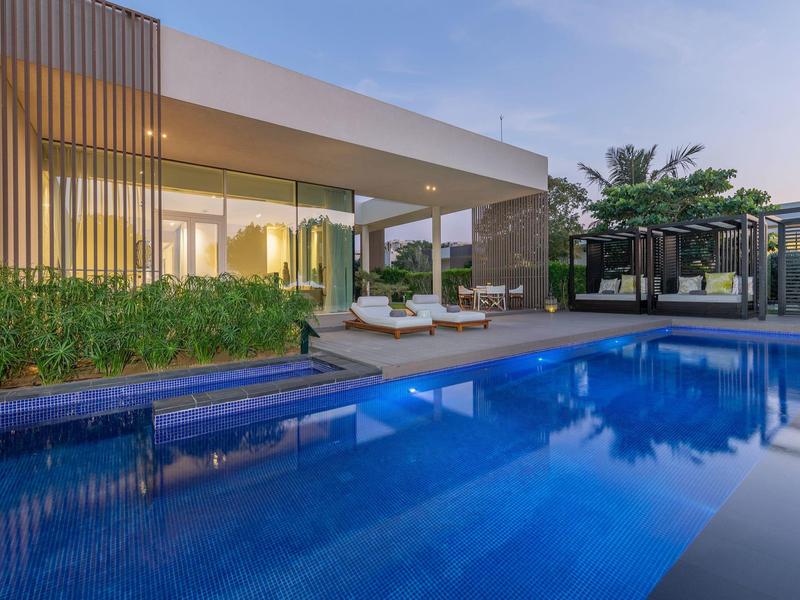 Moderner Poolbereich eines Hotels bei Sonnenuntergang mit Liegestühlen und üppigen Pflanzen.