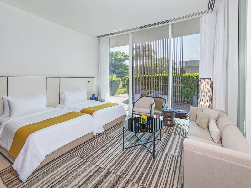 Helles Hotelzimmer mit großem Bett, Glaswand und modernem Sitzbereich mit Sofa und Tisch.