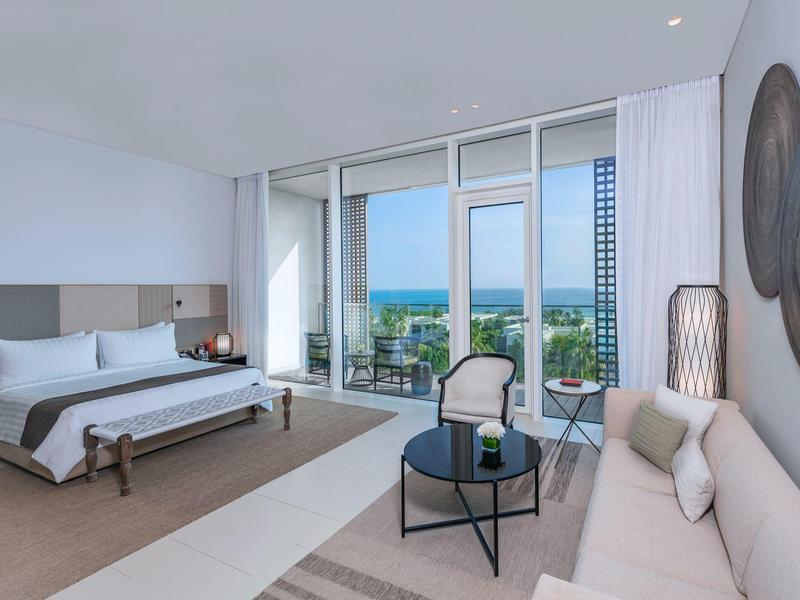 Modernes Hotelzimmer mit großem Bett, Sofa und Meerblick durch bodentiefe Fenster.