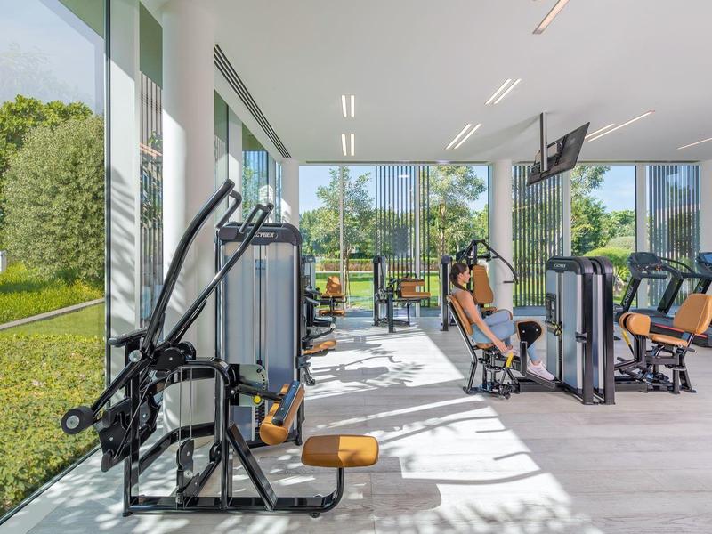 Moderner Fitnessraum mit Kraftgeräten und großen Fenstern mit Blick auf den Garten.