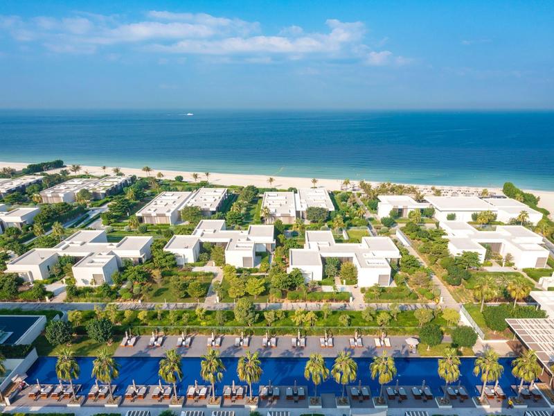 Luftaufnahme eines Hotels mit Pool, Gärten und Strand am Meer im Hintergrund.