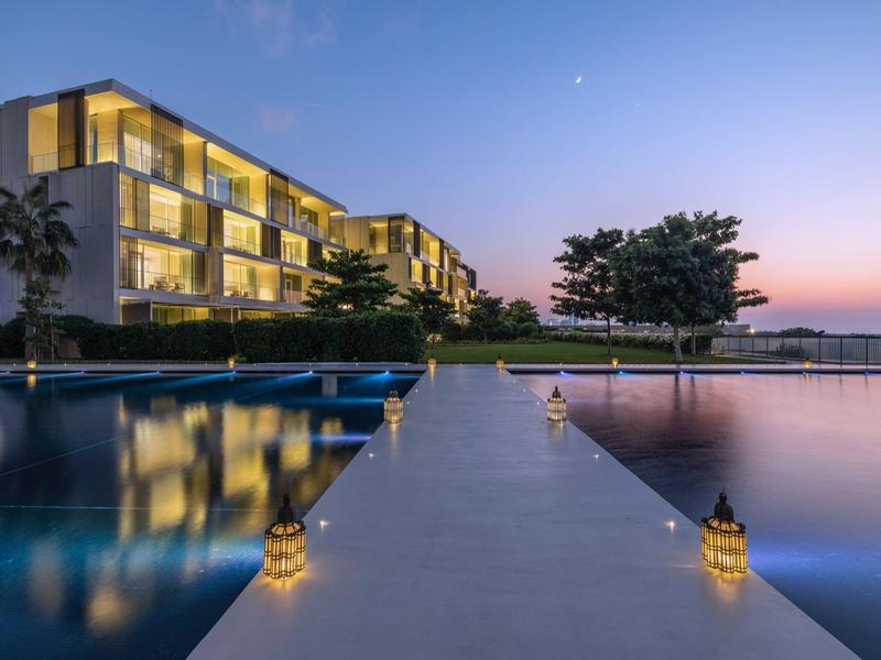 Moderner Hotelkomplex mit beleuchtetem Pool und Steg bei Sonnenuntergang.