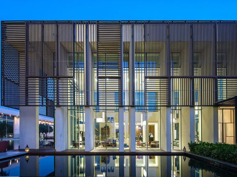 Modernes Hotelgebäude mit großen Glasfronten, beleuchtet am Abend neben einem Pool.