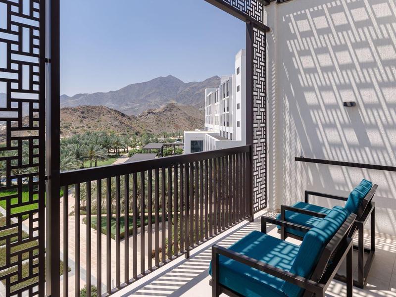 Balkon mit schwarzem Geländer, blauen Stühlen und Bergblick unter blauem Himmel am Tag.