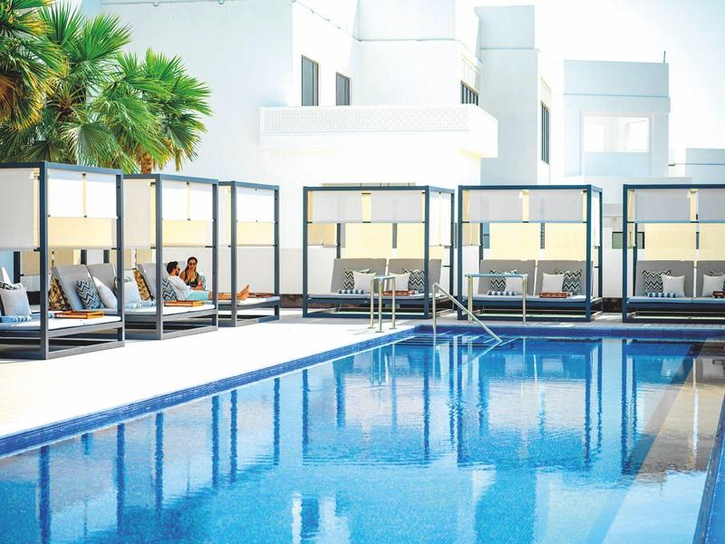 Moderner Pool mit blauer Wasseroberfläche, weißen Liegen und Palmen im Hintergrund.