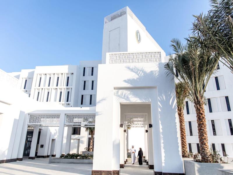 Großes weißes modernes Gebäude mit Palmen vor blauem Himmel und klarer Sonneneinstrahlung.