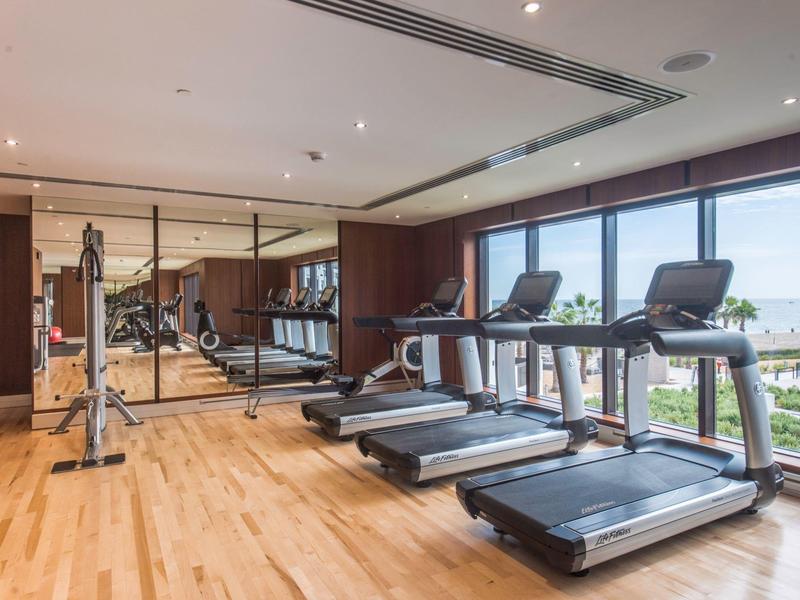 Moderner Fitnessraum mit Holzfußboden, drei Laufbändern und großen Fenstern mit Meerblick.