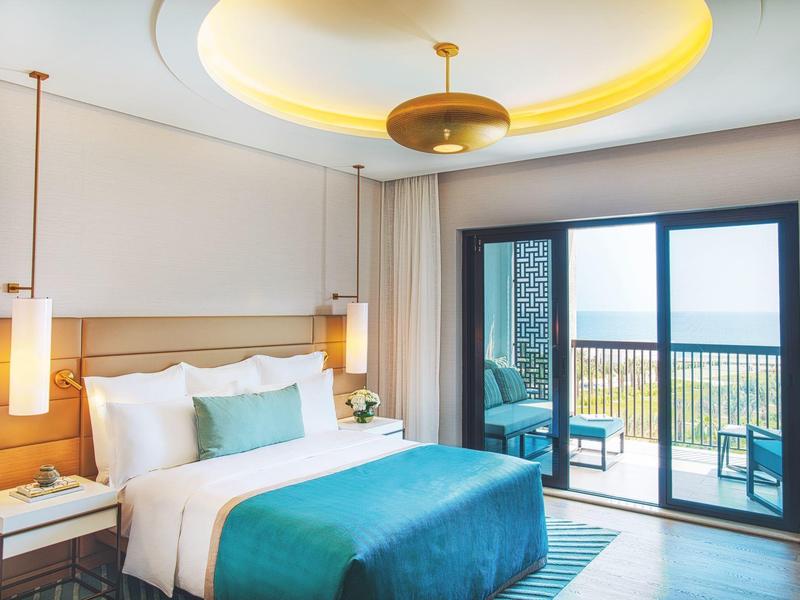 Modernes Schlafzimmer mit großem Bett, türkisfarbener Decke, Balkon und Meeresblick bei Tageslicht.