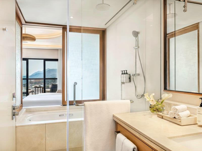 Helles Badezimmer mit Glasdusche, großem Spiegel, Naturholzakzenten und Blick ins Schlafzimmer.