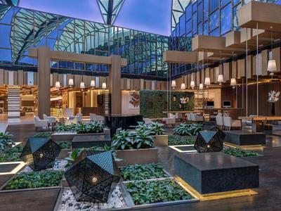 Moderne hotel lobby met planten, zitplaatsen en een glazen dak