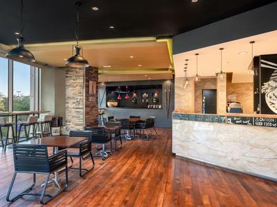 Moderní hotelová lounge s dřevěnou podlahou, jídelními stoly a velkými okny.