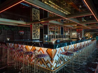 Moderní bar s geometrickými vzory, stoličkami a tmavou atmosférou v hotelu.
