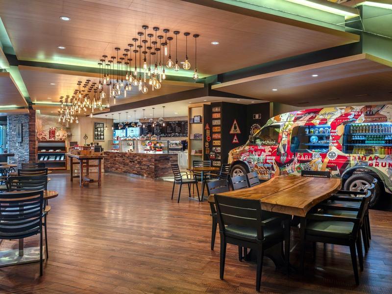 Moderne hotelbar met houten vloer, tafels, stoelen en kleurrijke muurschildering.