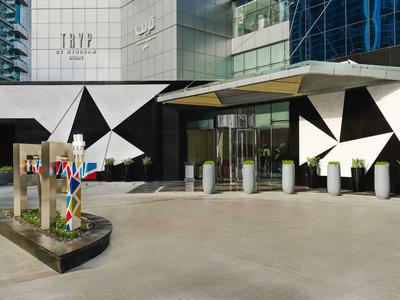 Entrada moderna del hotel con fachada geométrica en blanco y negro y escultura colorida en primer plano.