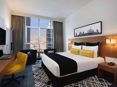 Habitación de hotel moderna con cama cómoda, escritorio, televisor y vista a la ciudad por ventana grande.