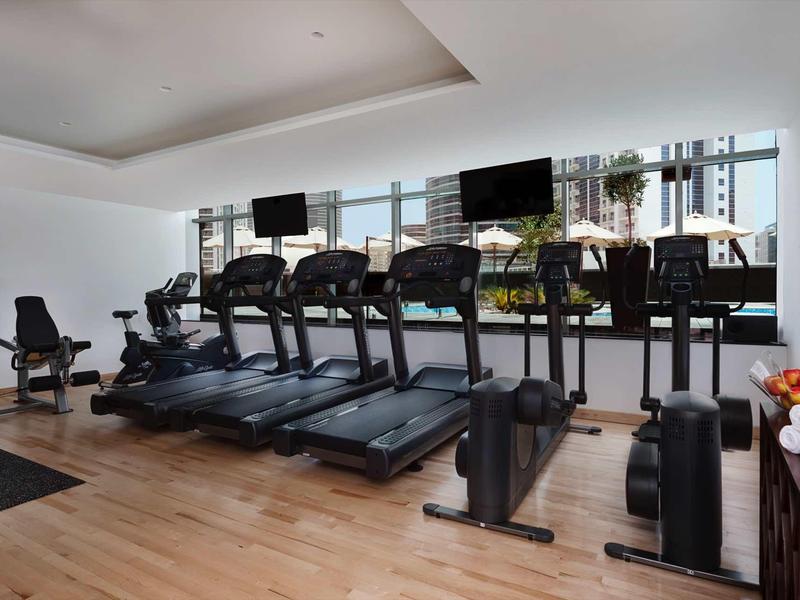 Gimnasio moderno con cintas de correr y bicicletas estáticas junto a ventanas grandes y suelo de madera.