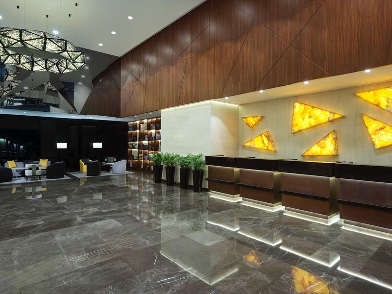 Área de lobby de hotel moderna con suelo de mármol oscuro, recepción iluminada y elementos decorativos en la pared.