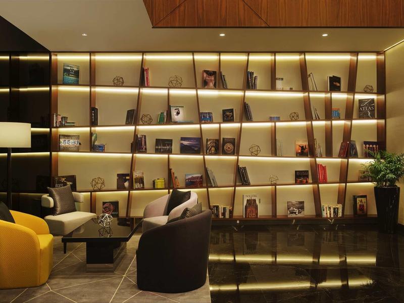 Lounge moderna de hotel con estantes iluminados, sillones coloridos y mesas de café.