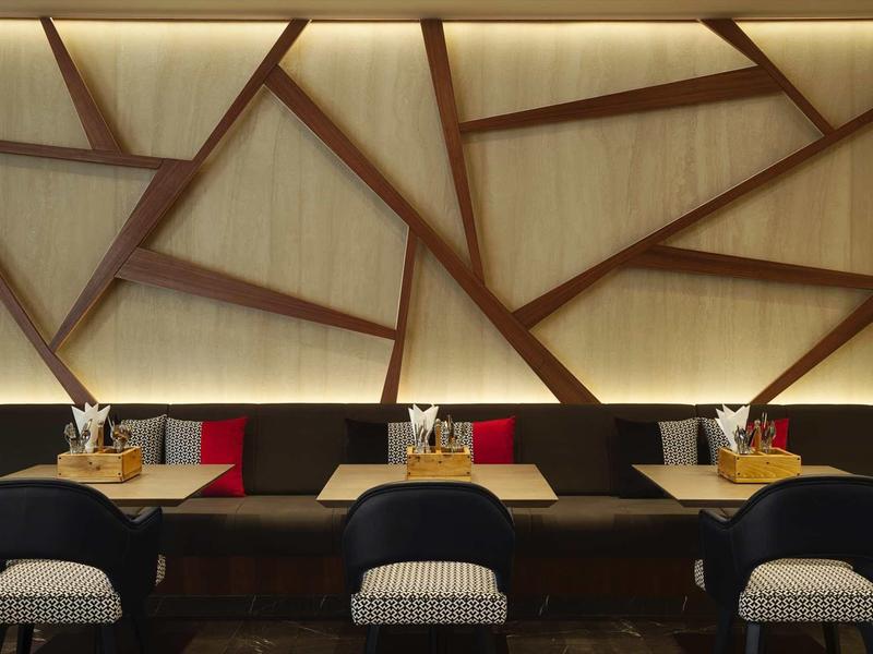 Pared de restaurante moderna con diseño geométrico de madera y mesas preparadas con sillas bajo luz cálida.