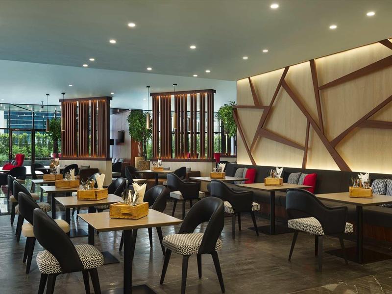 Área de restaurante de hotel moderno con mesas de madera, sillas cómodas y elementos de iluminación cálida.