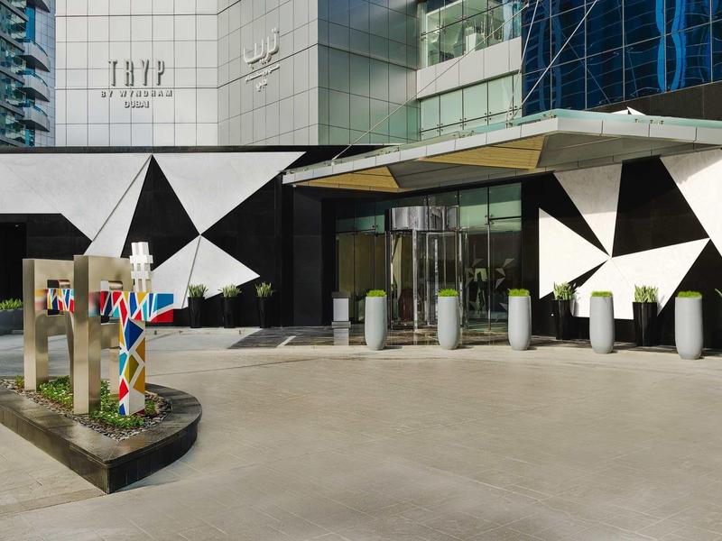 Entrada moderna del hotel con fachada geométrica en blanco y negro y escultura colorida en primer plano.