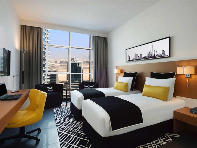 Habitación de hotel moderna con dos camas, escritorio, silla y ventana con vista a la ciudad.