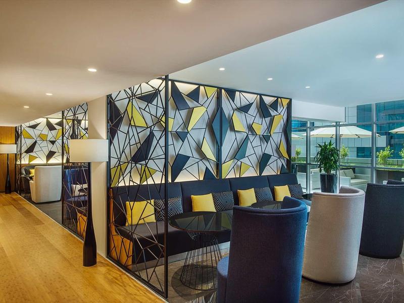 Lounge moderna de hotel con separadores geométricos, asientos cómodos y piso de madera.