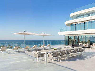 Modern hotel terrace with seating and lounge area overlooking the sea under a clear blue sky.