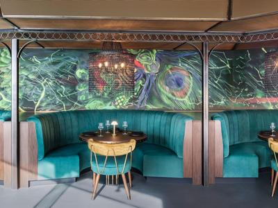 Modern restaurant with green interior and round wooden tables with chairs.