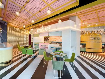 Moderner Café-Innenraum mit grünen Stühlen, weißen Tischen und gestreiftem Schwarz-Weiß-Boden.