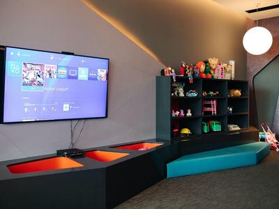 Moderner Spielbereich mit beleuchtetem Stauraum, Fernseher und bunten Spielsachen auf Regalen.