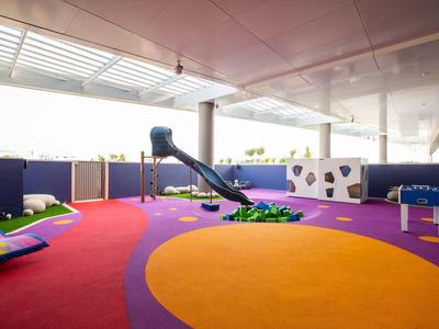 Hell überdachter Kinder-Spielbereich mit weichem Boden, Rutsche und Kletterwand in bunten Farben.