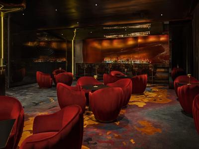 Dunkle Bar mit roten Sesselgruppen, gedämpfter Beleuchtung und gemustertem Teppichboden.