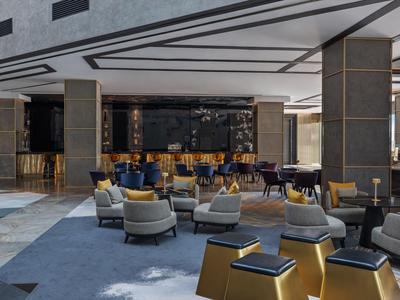 Moderne Hotellobby mit grauen Sesseln, blauen Teppichen und dunklen Holzmöbeln.