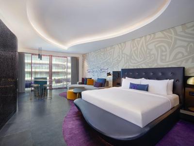 Modernes Hotelzimmer mit großem Bett, lila Teppich, geschwungener Decke und Panoramafenster.