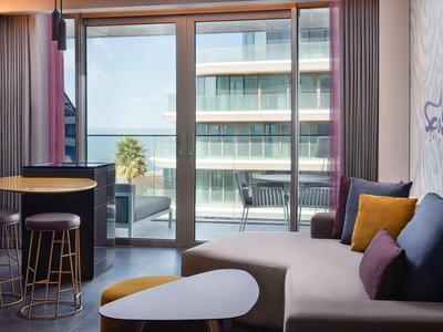 Moderner Wohnraum mit Sofa, bunten Kissen, Tisch und Balkon mit Blick auf moderne Gebäude.