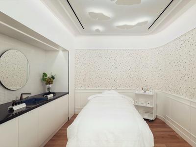 Světlá masážní místnost s bílou postelí, kulatým zrcadlem a minimalistickým dekorem.