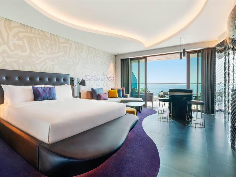 Modernes Hotelzimmer mit großem Bett, stilvollen Möbeln und Panoramafenster mit Meerblick.