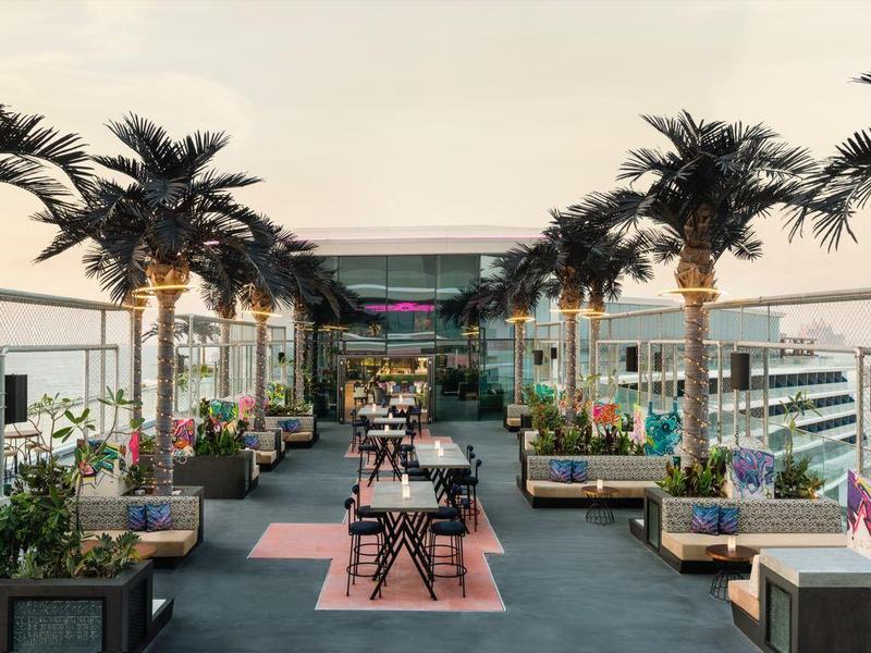 Dachterrasse mit Palm Bäumen, Sitzgruppen, modernen Möbeln und Meerblick bei Sonnenuntergang.