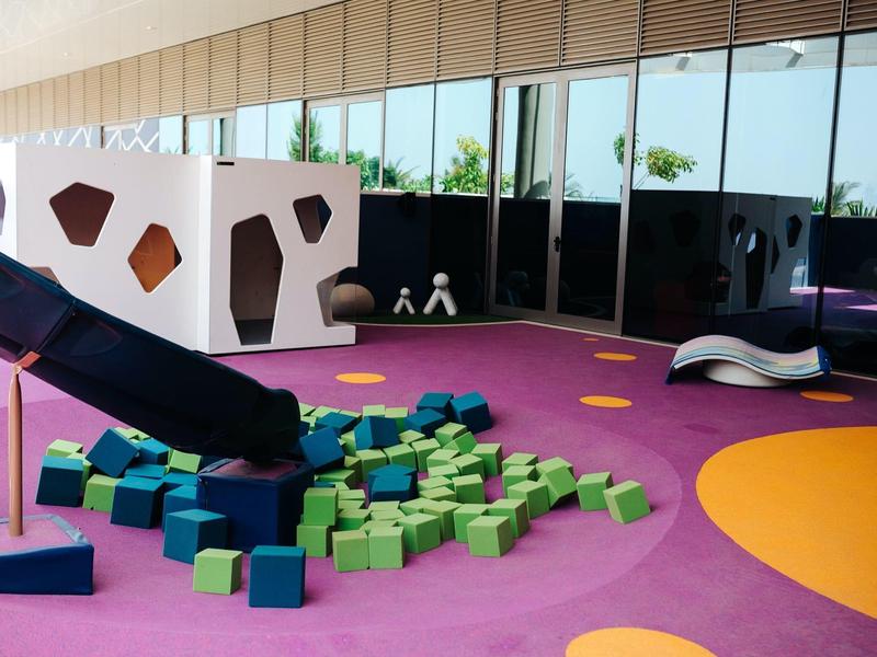 Bunter Indoor-Spielbereich mit Schaumstoffwürfeln, großer weißer Kletterstruktur und Rutsche.