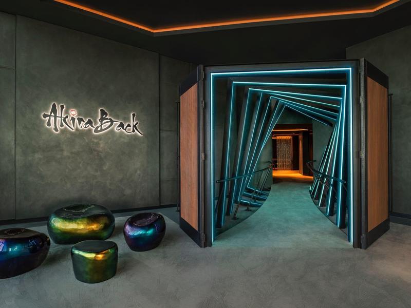 Moderner Eingangsbereich mit beleuchtetem Kunstwerk, bunten Sitzkissen und geometrischem Tunnel.