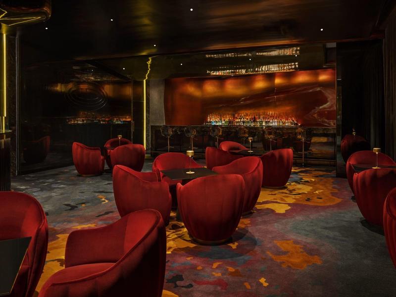 Dunkle Bar mit roten Sesselgruppen, gedämpfter Beleuchtung und gemustertem Teppichboden.